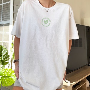 May include: White oversized t-shirt with a green flower graphic and the text "We're gonna be alright".