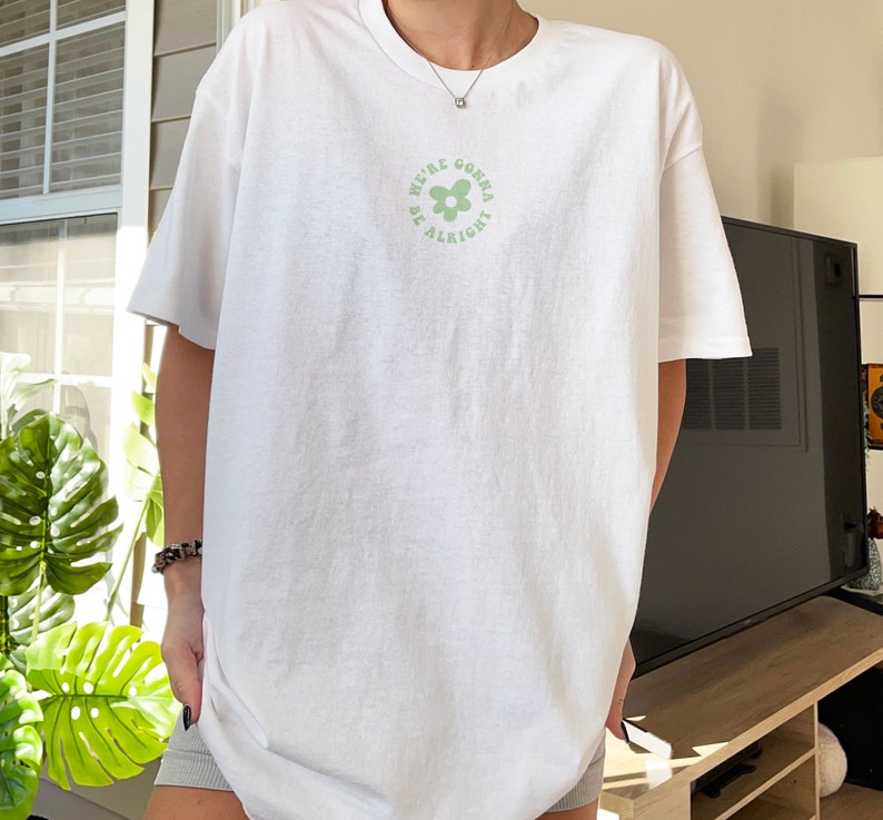 May include: White oversized t-shirt with a green flower graphic and the text "We're gonna be alright".