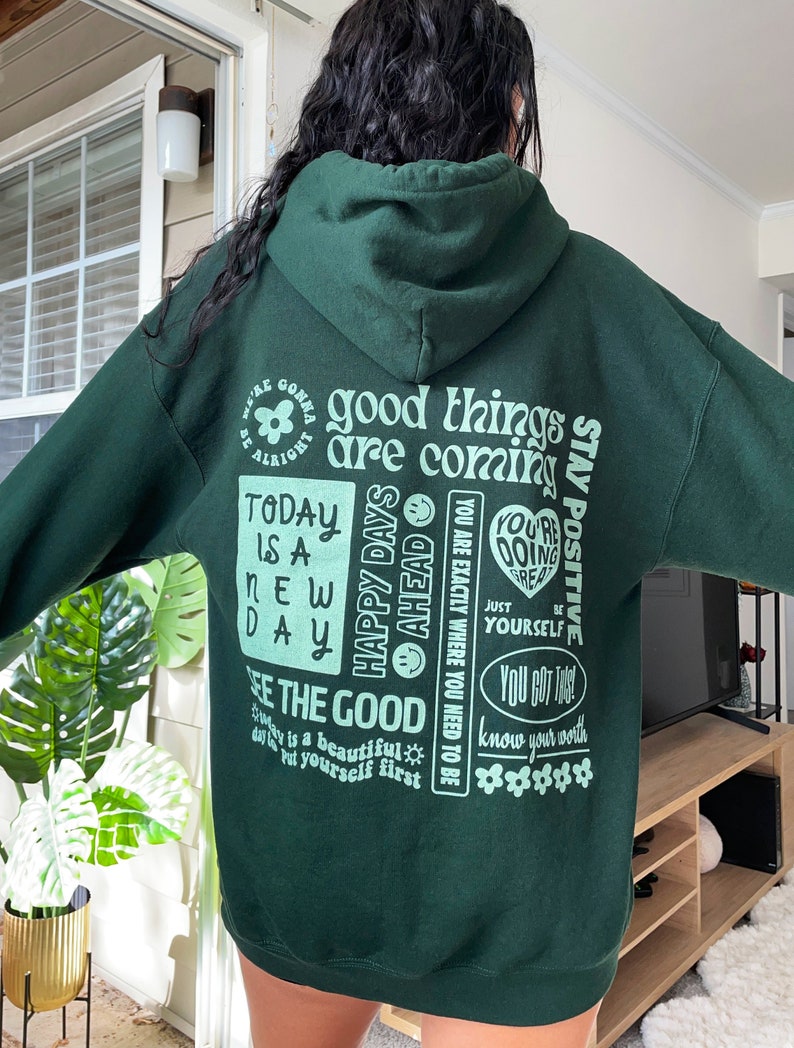 May include: Green hooded sweatshirt with a variety of positive affirmations printed on the back, including "good things are coming", "stay positive", "happy days ahead", "today is a new day", "see the good", "you are exactly where you need to be", "you're doing great", "just be yourself", "you got this", and "know your worth".