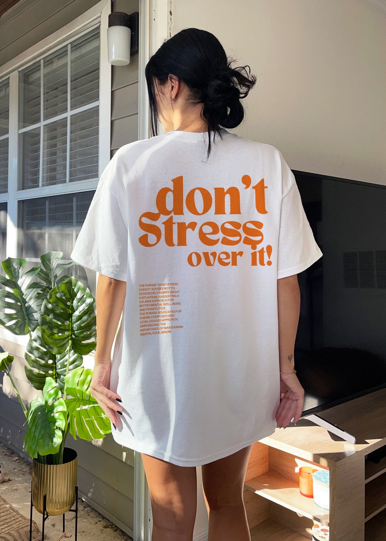 Puede incluir: Camiseta blanca de gran tama&ntilde;o con el texto "don't stress over it!" impreso en naranja en la parte posterior. El texto est&aacute; en una fuente en negrita y retro.