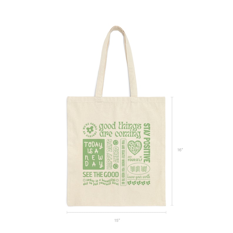 May include: A beige canvas tote bag with green text that reads "good things are coming", "today is a new day", "happy days ahead", "see the good", "you are exactly where you need to be", "you're doing great", "just be yourself", "you got this", "know your worth", and "stay positive". The bag is 15 inches wide and 16 inches tall.