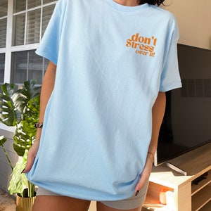 Puede incluir: Una camiseta azul claro con el texto "don't stress over it!" en naranja.