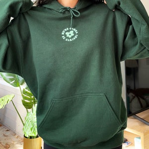 May include: A dark green hooded sweatshirt with a flower graphic and the text "We're gonna be alright".
