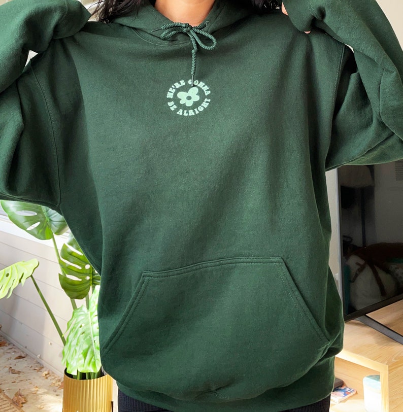 May include: A dark green hooded sweatshirt with a flower graphic and the text "We're gonna be alright".