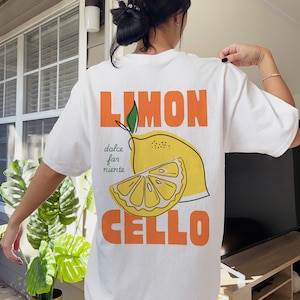 May include: White t-shirt with a graphic of a lemon and the text "LIMON CELLO" in orange. The text "dolce far niente" is written in green below the lemon.