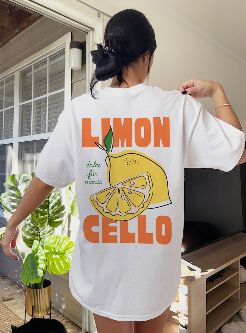May include: White t-shirt with a graphic of a lemon and the text "LIMON CELLO" in orange. The text "dolce far niente" is written in green below the lemon.