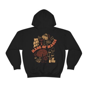 May include: Black hooded sweatshirt with a mushroom graphic and the text "WE ARE ALL MADE OF MAGIC BE YOU". The design features various mushroom illustrations in shades of brown and orange.