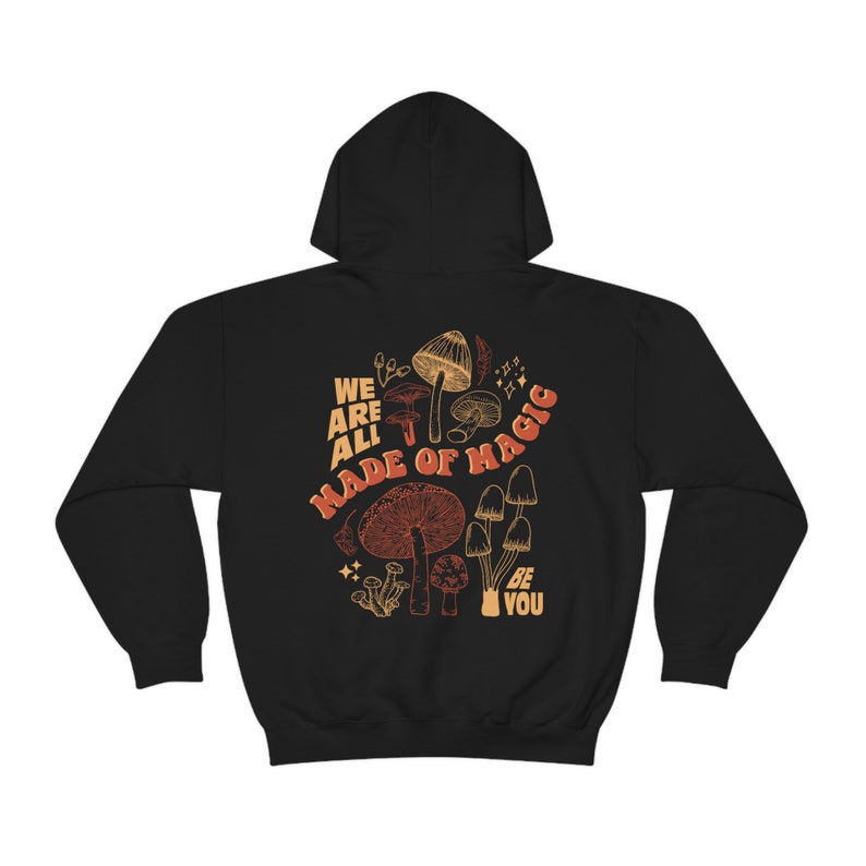May include: Black hooded sweatshirt with a mushroom graphic and the text "WE ARE ALL MADE OF MAGIC BE YOU". The design features various mushroom illustrations in shades of brown and orange.