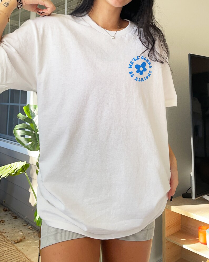 May include: White oversized t-shirt with a blue graphic of a flower and the text "We're gonna be alright".