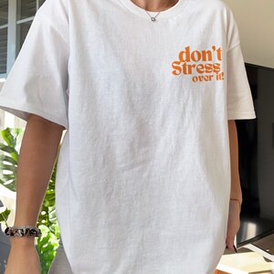 Puede incluir: Camiseta blanca de gran tama&ntilde;o con el texto "don't stress over it" en naranja.