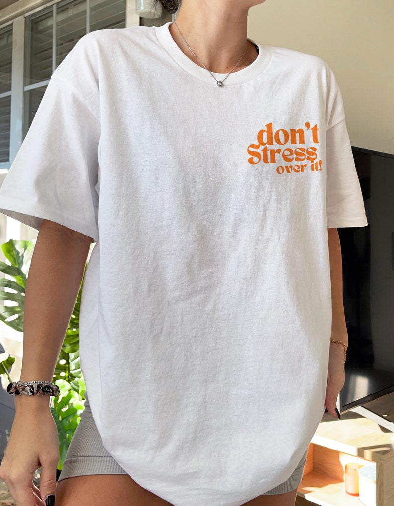 Puede incluir: Camiseta blanca de gran tama&ntilde;o con el texto "don't stress over it" en naranja.