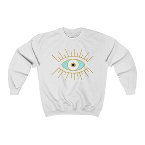 May include: White sweatshirt with a gold evil eye design. The eye is blue with a black pupil.