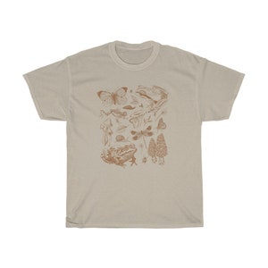 May include: A beige t-shirt with a brown graphic print of various forest creatures, including butterflies, frogs, mushrooms, and dragonflies.