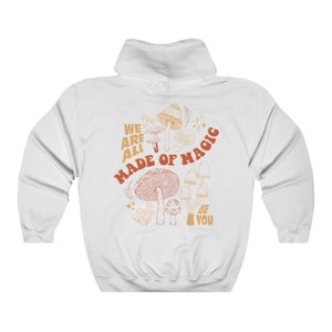 May include: White hooded sweatshirt with a mushroom graphic on the back. The design features various mushroom illustrations in shades of orange and brown, with the text "WE ARE ALL MADE OF MAGIC" and "BE YOU".