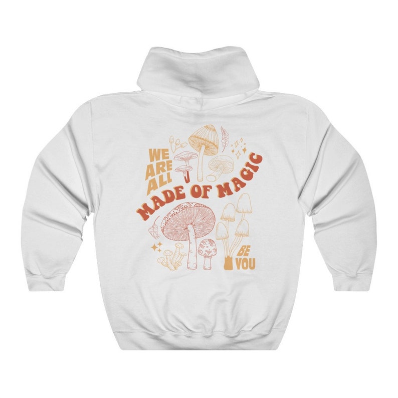May include: White hooded sweatshirt with a mushroom graphic on the back. The design features various mushroom illustrations in shades of orange and brown, with the text "WE ARE ALL MADE OF MAGIC" and "BE YOU".
