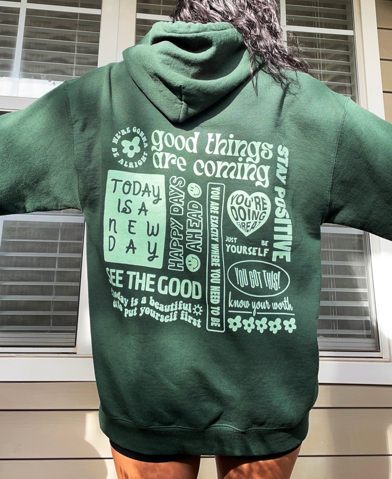 May include: Green hooded sweatshirt with a variety of positive messages printed on the back in a light green color. The text includes "good things are coming", "today is a new day", "happy days ahead", "you're doing great", "see the good", "you got this", and "know your worth".