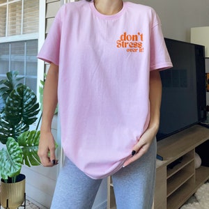 Puede incluir: Una camiseta rosa con el texto "don't stress over it" en naranja.