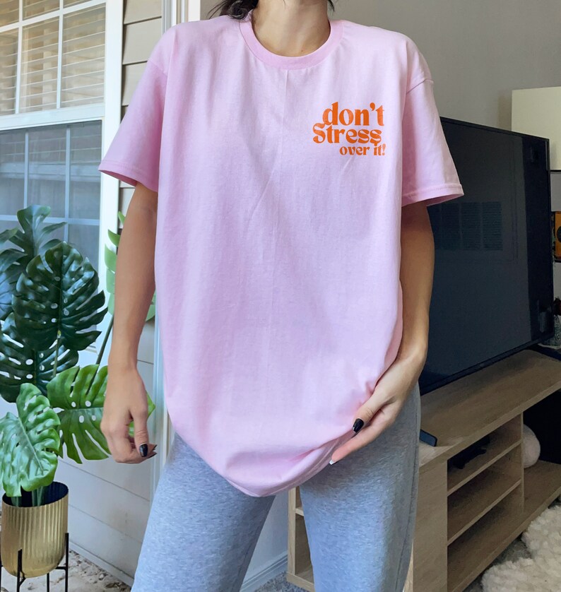 Puede incluir: Una camiseta rosa con el texto "don't stress over it" en naranja.
