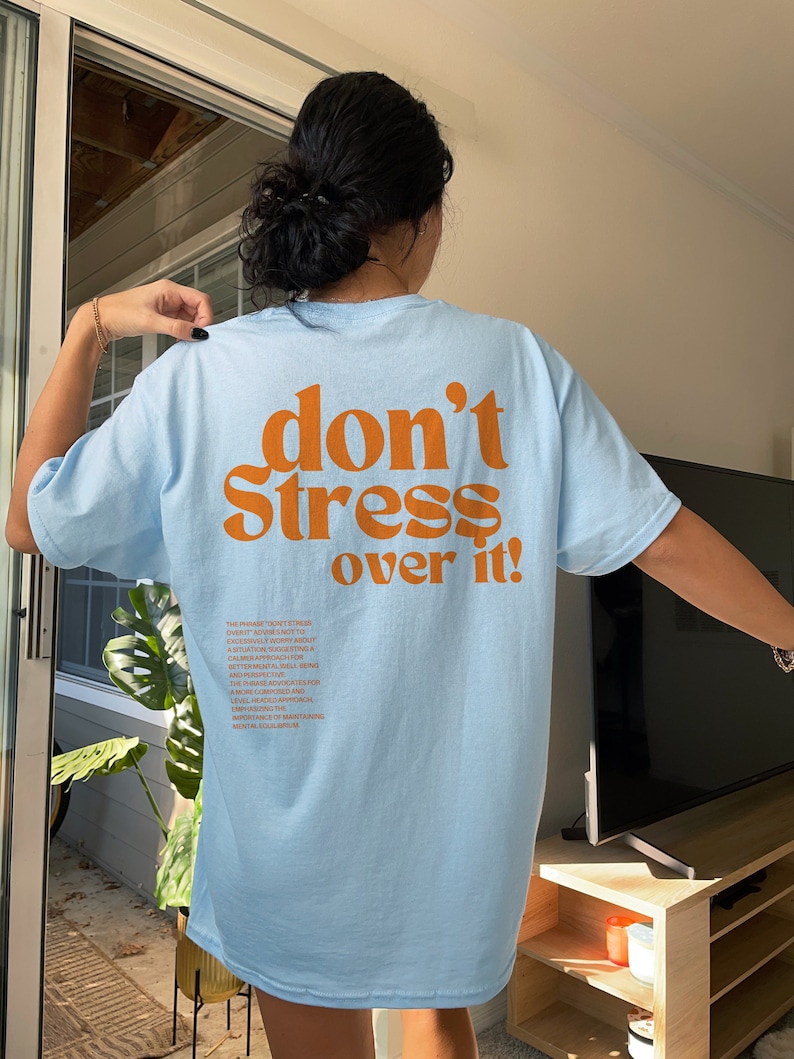 Puede incluir: Camiseta azul claro con el texto "don't stress over it!" impreso en naranja en la parte posterior. El texto est&aacute; en una fuente retro en negrita. La frase "don't stress over it" es un recordatorio para mantener la calma y la relajaci&oacute;n.