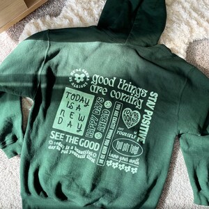 May include: Green hooded sweatshirt with a light green print of positive affirmations, including "good things are coming", "happy days ahead", "see the good", "you got this", and "stay positive".