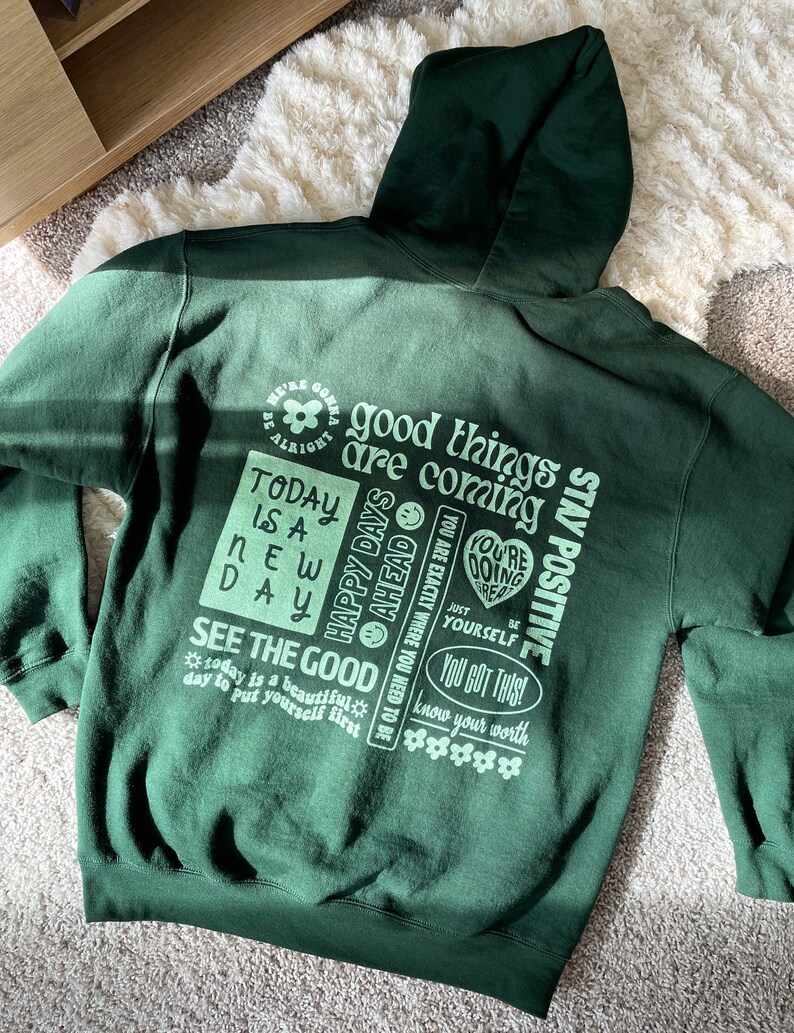 May include: Green hooded sweatshirt with a light green print of positive affirmations, including "good things are coming", "happy days ahead", "see the good", "you got this", and "stay positive".