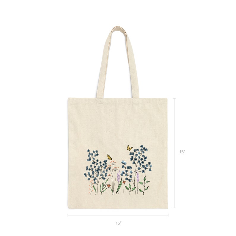 K&ouml;nnte beinhalten: Eine beige Canvas-Tragetasche mit einem Blumendesign mit blauen Blumen, gr&uuml;nen Bl&auml;ttern und gelben Schmetterlingen. Die Tasche ist 38 cm breit und 41 cm hoch.