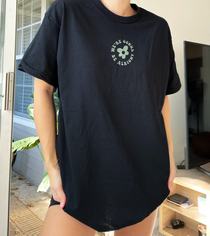 May include: Black t-shirt with a green flower graphic and the text "We're gonna be alright" in a circle.