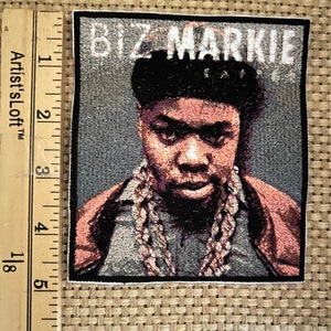 Puede incluir: Un parche bordado en blanco y negro con un retrato de Biz Markie, un rapero, con el texto "Biz Markie" sobre su cabeza.