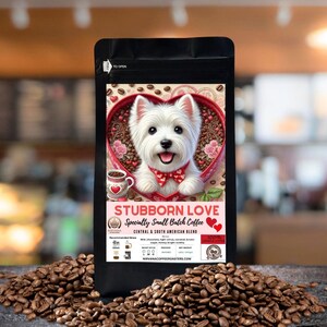 May include: A bag of coffee beans with a label that says "Stubborn Love" and features a white dog with a red bow tie inside a heart-shaped box. The label also says "Specialty Small Batch Coffee" and "Central & South American Blend".