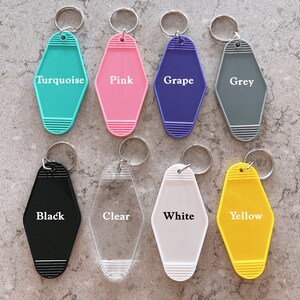 May include: Eight motel-style keychains arranged in two rows. The top row features turquoise, pink, grape, and grey colors. The bottom row includes black, clear, white, and yellow. Each keychain has a metal ring and horizontal ribbed details.