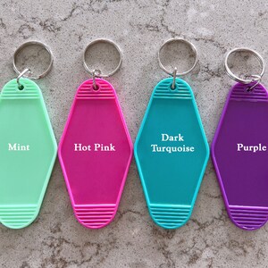 May include: Four motel-style plastic keychains with metal rings, each featuring a distinct color and printed text: Mint, Hot Pink, Dark Turquoise, and Purple. The keychains have a diamond-like shape with horizontal ribbed detailing at the top and bottom.