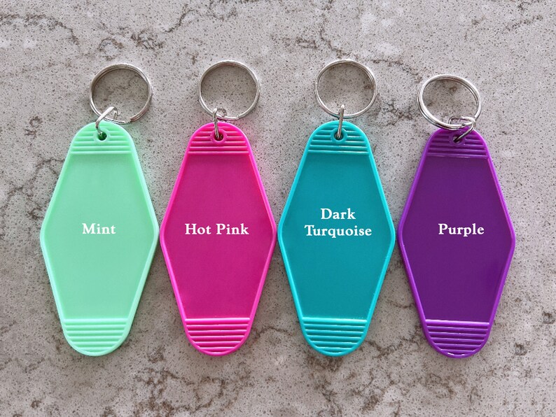May include: Four motel-style plastic keychains with metal rings, each featuring a distinct color and printed text: Mint, Hot Pink, Dark Turquoise, and Purple. The keychains have a diamond-like shape with horizontal ribbed detailing at the top and bottom.