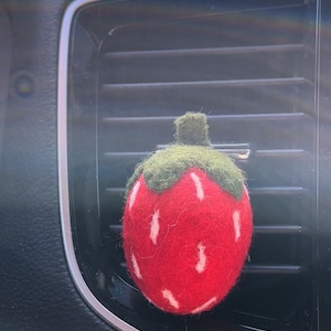 May include: A red felt strawberry car air freshener with white accents and a green felt stem and leaves.