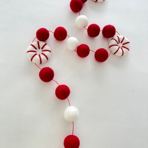 May include: A red and white felt garland with peppermint candy ornaments. The garland is strung with red and white pom poms.