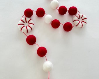 May include: A red and white felt garland with peppermint candy ornaments. The garland is strung with red and white pom poms.