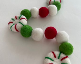 May include: A festive garland made of felt balls in red, white, and green. The garland features peppermint candy designs.