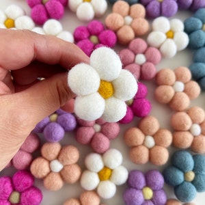 May include: A collection of felt flower embellishments in various colors, including pink, blue, white, and peach. The flowers have a simple, five-petal design and are perfect for adding a touch of whimsy to crafts and projects.