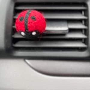 May include: A red and black ladybug-shaped car air freshener hanging from a car's air vent.