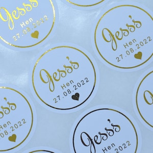 Puede incluir: Una colecci&oacute;n de pegatinas circulares blancas con texto en l&aacute;mina dorada que dice Jess's Hen 27.08.2022, acompa&ntilde;ado de un peque&ntilde;o icono de coraz&oacute;n dorado. Cada pegatina tiene un borde dorado y el dise&ntilde;o se repite en la hoja en cuadr&iacute;cula.