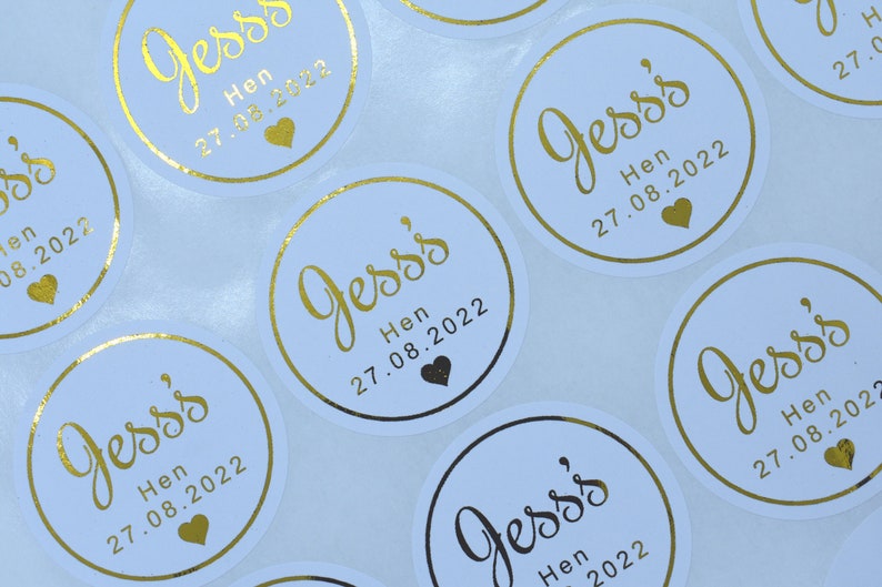 Puede incluir: Una colecci&oacute;n de pegatinas circulares blancas con texto en l&aacute;mina dorada que dice Jess's Hen 27.08.2022, acompa&ntilde;ado de un peque&ntilde;o icono de coraz&oacute;n dorado. Cada pegatina tiene un borde dorado y el dise&ntilde;o se repite en la hoja en cuadr&iacute;cula.