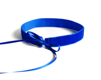 May include: A blue velvet ribbon tied in a bow. The ribbon is about 1 inch wide and is lying on a white background.
