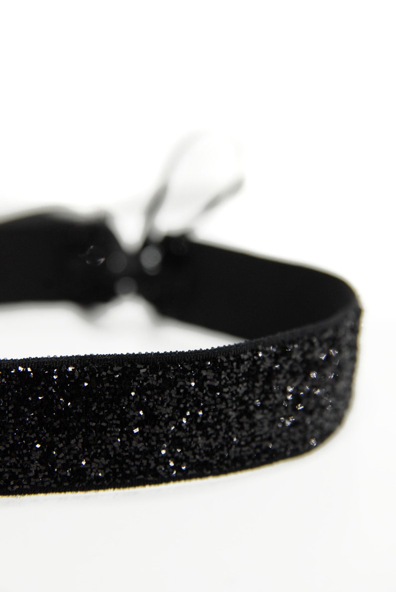 Schwarzer, funkelnder, 1,5cm breiter Choker. Der Samtchoker ist dehnbar und wird individuell mit zwei hochwertigen Double Face Satinbändern gebunden. Das perfekte Halsband für die nächste Party.