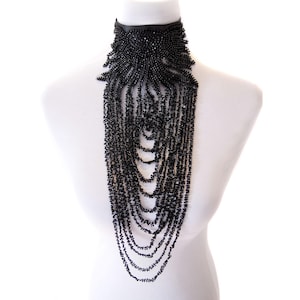 Könnte beinhalten: Eine schwarze Perlenkette mit einem Halsband-Stil und kaskadierenden Perlensträngen. Die Halskette wird auf einer weißen Mannequin-Büste präsentiert, die ihr aufwendiges Design und ihren eleganten Fall zeigt. Die Perlen sind klein und gleichmäßig.