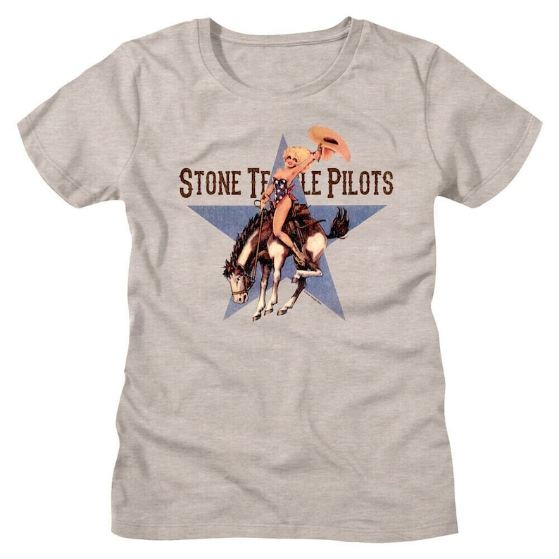 Op de afbeelding: Een grijs T-shirt met een blauwe ster en de tekst "Stone Temple Pilots" in wit. Een vrouw in badkleding rijdt op een paard in de ster.