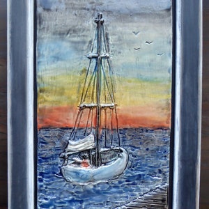 Könnte beinhalten: Ein gerahmtes Keramikfliesen-Kunstwerk, das ein Segelboot auf einem Gewässer mit einem Sonnenuntergang im Hintergrund zeigt. Die Fliese ist signiert mit "L.Tichy" und datiert mit "2018".