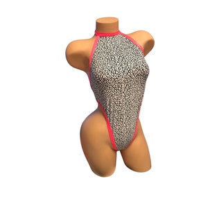 May include: A high-cut, halter-neck swimsuit with a black and white animal print. The edges and halter strap are trimmed with bright pink. The swimsuit is displayed on a mannequin.