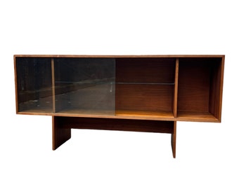 May include: A mid-century modern wooden bookcase with glass doors and open shelves. The bookcase is made of dark wood and has a simple, elegant design.