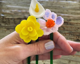Könnte beinhalten: Ein Strauß aus drei Glasblumen mit grünen Stielen. Die Blumen sind eine gelbe Narzisse, eine rosa und violette Blume und eine weiße Calla.