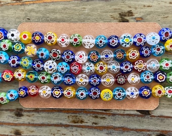 Könnte beinhalten: Nahaufnahme einer Karte mit Reihen von bunten Glasperlen. Die Perlen sind rund und haben ein Blumenmuster. Die Perlen sind in einem Muster aus abwechselnden Farben angeordnet.
