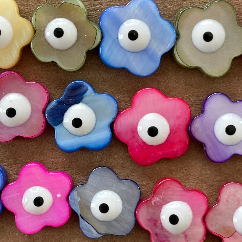 May include: Assortment of colorful flower-shaped charms with a blue evil eye design. Each charm has a different color and pattern, including pink, blue, purple, and green.